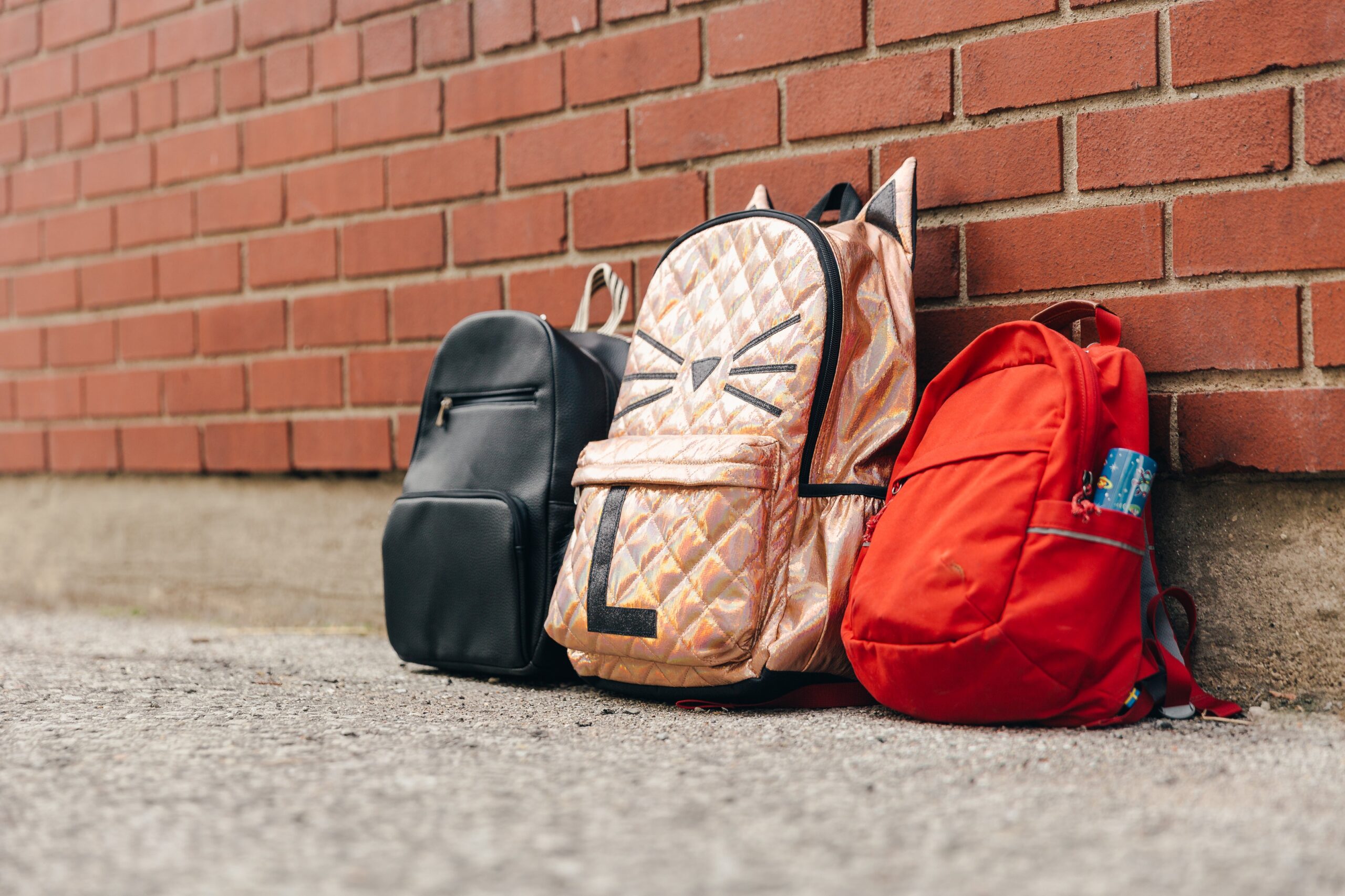 Três mochilas infantis e uma parede de tijolo